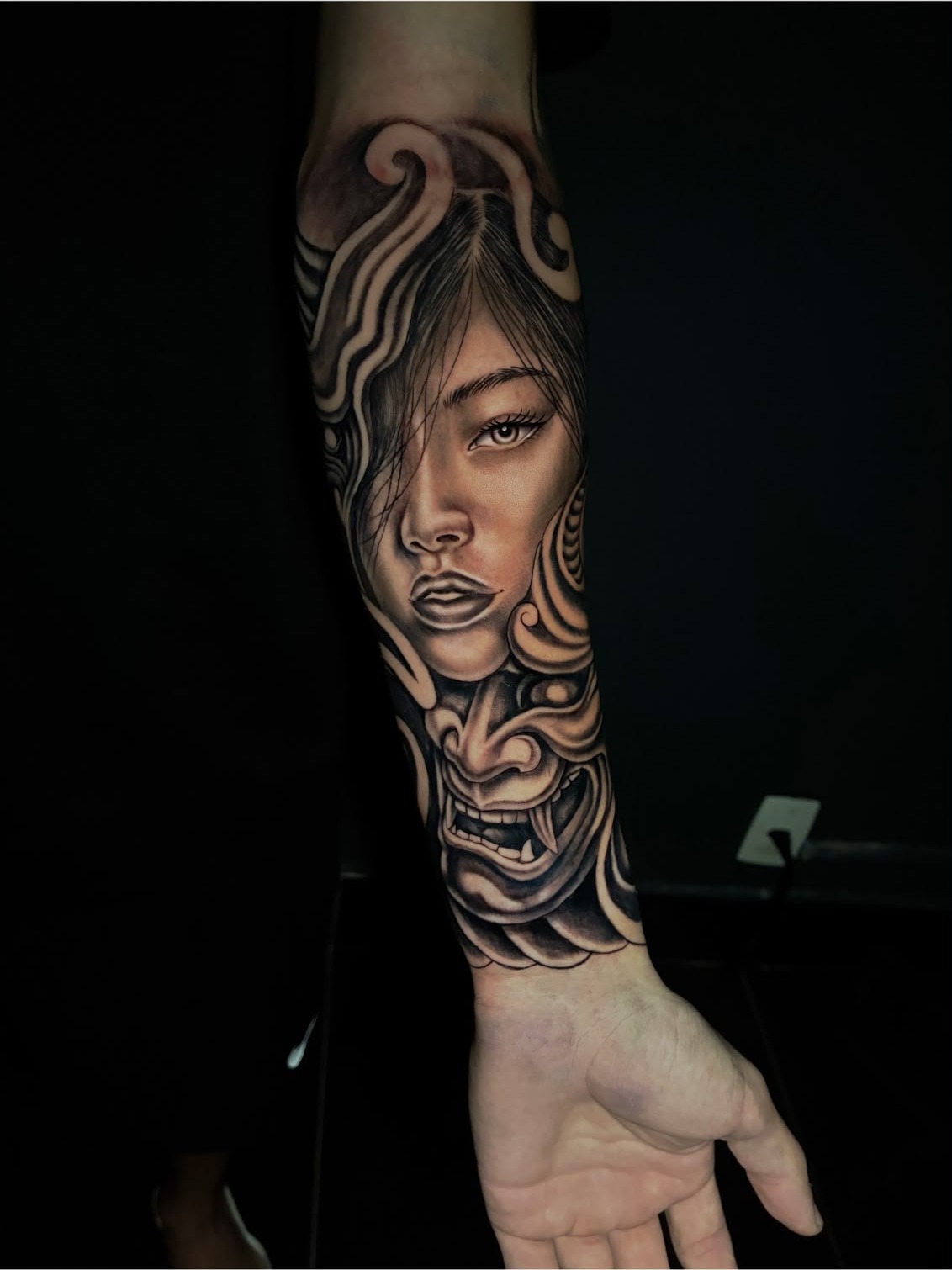 Tatuagem realista em preto e cinza de rosto feminino com máscara hannya no antebraço